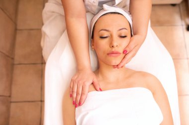 Masözün nazik elleri, masaj masasında oturan orta yaşlı bir kadına masaj yapıyor.