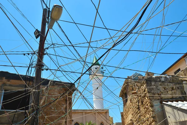 Power lines, a messy mess of power lines between houses in the ancient Phoenician city of Tyros in Lebanon. Part of the mosque is visible in the background.