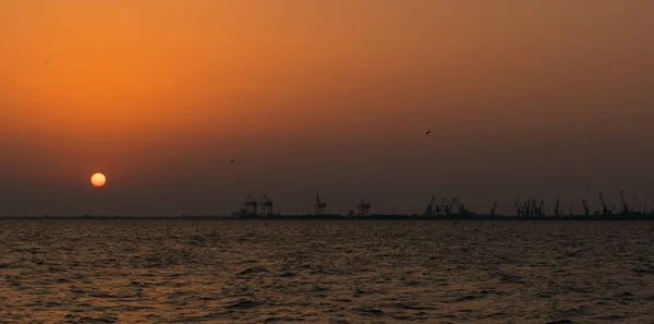 Deniz gün batımı ve Selanik liman vinçleri