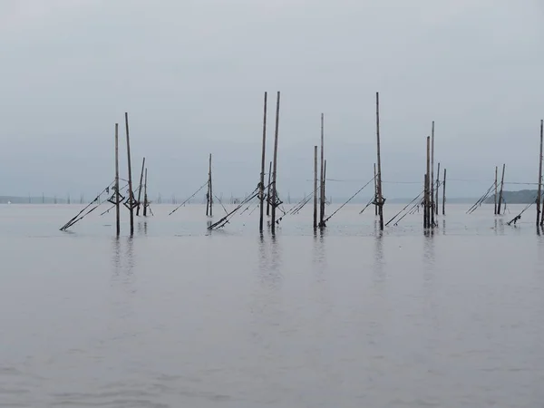 Bamboo poles adhered to the net for catch fish reflection in the water sea environment background