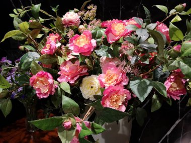 Beyaz bir vazoda pembe ve sarı güller, ahşap bir masa üzerinde siyah mermer arka plan, yapay çiçekler.