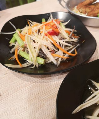 Yeşil papaya salatası siyah tabağa turşulu yengeç, meyve ve sebze taze Tayland yemeği ekşi tatlı tuzlu tatlı