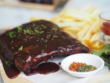 BBQ soslu ızgara domuz pirzolası ve balda karamelize edilmiş patates kızartması. Tahta tabakta.