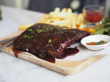 BBQ soslu ızgara domuz pirzolası ve balda karamelize edilmiş patates kızartması. Tahta tabakta.