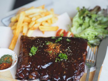 BBQ soslu ızgara domuz pirzolası ve balda karamelize edilmiş patates kızartması. Tahta tabakta.