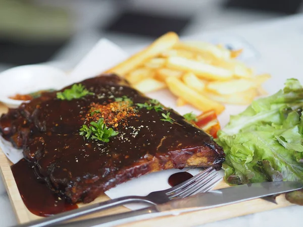 BBQ soslu ızgara domuz pirzolası ve balda karamelize edilmiş patates kızartması. Tahta tabakta.