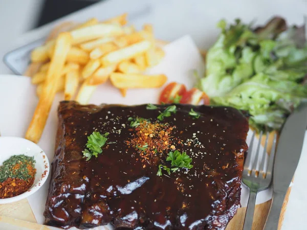 BBQ soslu ızgara domuz pirzolası ve balda karamelize edilmiş patates kızartması. Tahta tabakta.