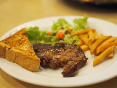Sebze salatalı kara biber domuzu, kızarmış ekmek ve yemek için pişirilmiş beyaz tabakta patates kızartması.