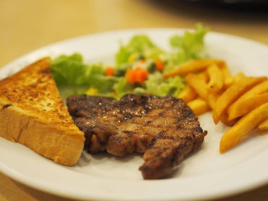 Sebze salatalı kara biber domuzu, kızarmış ekmek ve yemek için pişirilmiş beyaz tabakta patates kızartması.