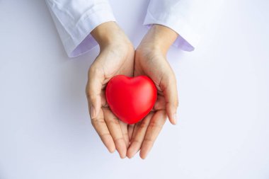 Kadın doktor elleri beyaz arka planda kırmızı kalbi tutuyor. 