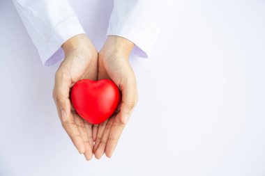 Kadın doktor elleri beyaz arka planda kırmızı kalbi tutuyor. 