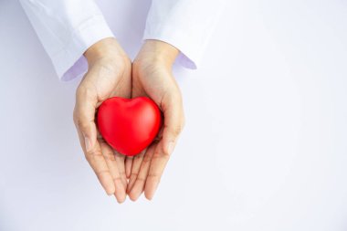Kadın doktor elleri beyaz arka planda kırmızı kalbi tutuyor. 