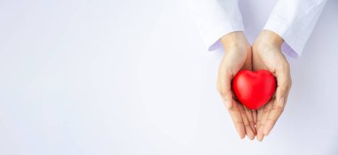 Kadın doktor elleri beyaz arka planda kırmızı kalbi tutuyor. 