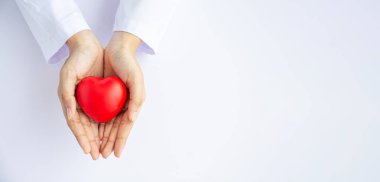 Kadın doktor elleri beyaz arka planda kırmızı kalbi tutuyor. 