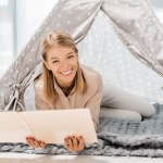 Mulher alegre segurando livro e olhando para a câmera no bebê wigwam