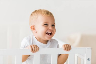 cheerful toddler standing in baby crib on white background clipart