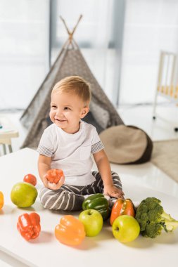 meyve ve sebze çevrili masada oturan sevimli gülümseyen toddler