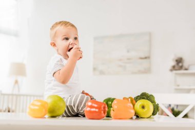 yemek ve meyve ve sebze çevrili masada oturan sevimli yürümeye başlayan çocuk