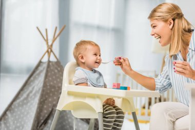 neşeli Anne oğlu sandalyesi kreş odasında bebek gıda ile besleme