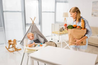 yiyecek taşıyan ve oğlu bebek sandalyede bakarak anne