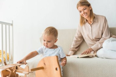 arka plan üzerinde anne ile çocuk odasında oyuncak ahşap oyuncak uçak ile oynarken mutlu yürümeye başlayan çocuk