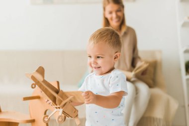 arka plan üzerinde anne ile çocuk odasında oyuncak ahşap oyuncak uçak ile oynarken mutlu yürümeye başlayan çocuk