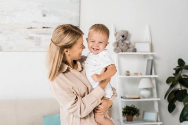neşeli anne holding gülümseyen oğul kreş odasında