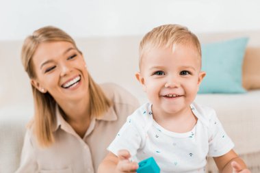 gülümseyen ve annesi ile kapalı kameraya bakarken oynayan sevimli yürümeye başlayan çocuk 