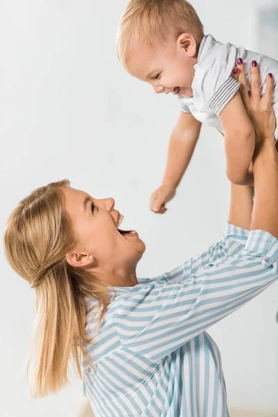 陽気な母の幼児を見て 白い背景の上の手で彼を保持 — ストック写真