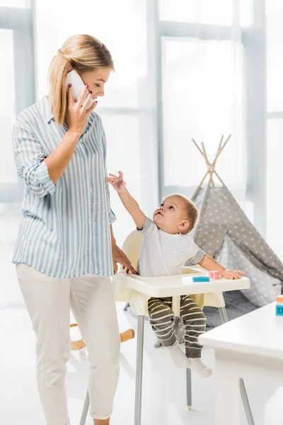 Madre Hablando Teléfono Inteligente Mientras Que Hijo Sentado Trona Habitación — Foto de Stock