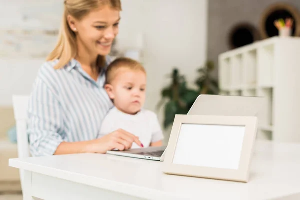 Mutter Sitzt Schreibtisch Mit Niedlichem Kleinkind Während Sie Laptop Benutzt — Stockfoto