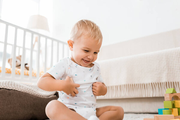 очаровательный ребенок улыбается и сидит на полу с красочными кубиками в детской комнате
