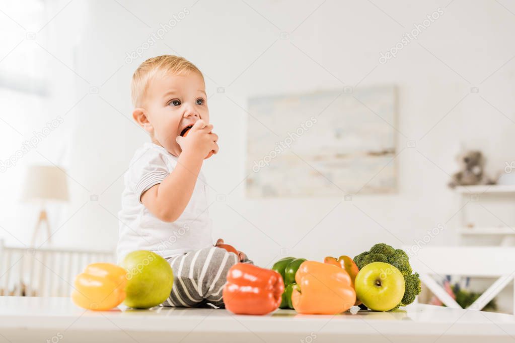 cute toddler eating and sitting on table surrounded by fruit and vegetables
