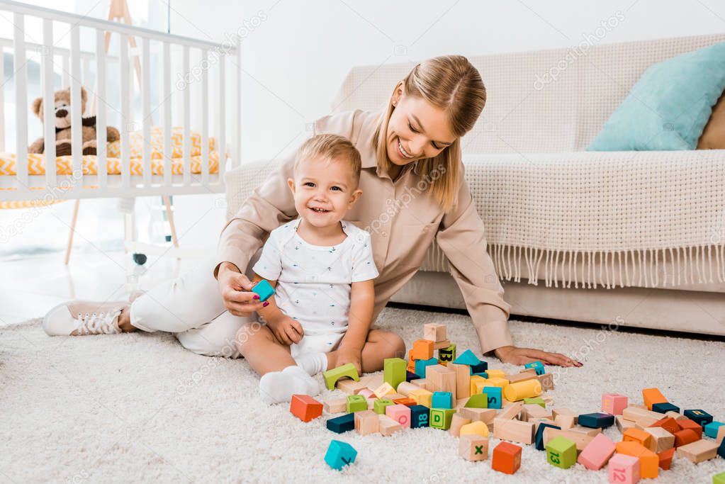adorable toddler playing with colorful cubes and mother in nursery room