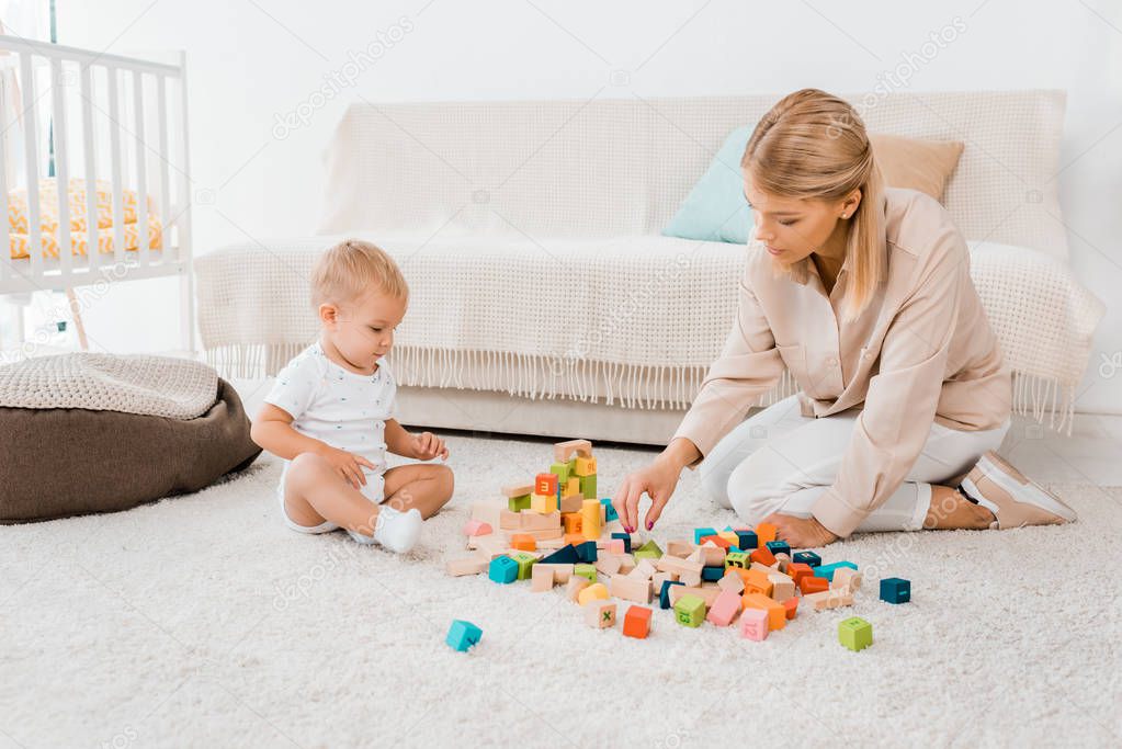 adorable toddler playing with colorful cubes and mother in nursery room