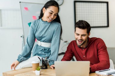 gülümseyen çok ırklı meslektaşları ofiste dizüstü bilgisayar kullanarak