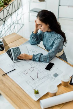 stressed asian female architect having headache while using laptop in office clipart