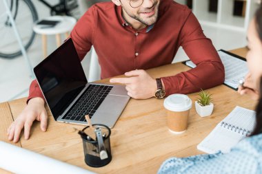 masada oturan ve Office boş ekran ile dizüstü bilgisayar kullanarak meslektaşlarının kırpılmış görünümü