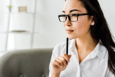 Güzel Asyalı işkadını formal giyim ve kalem tutan ve uzak ofis seyir gözlük