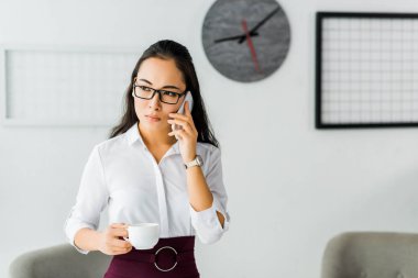 ofiste kahve molası verirken akıllı telefonda konuşan güzel ciddi asyalı iş kadını