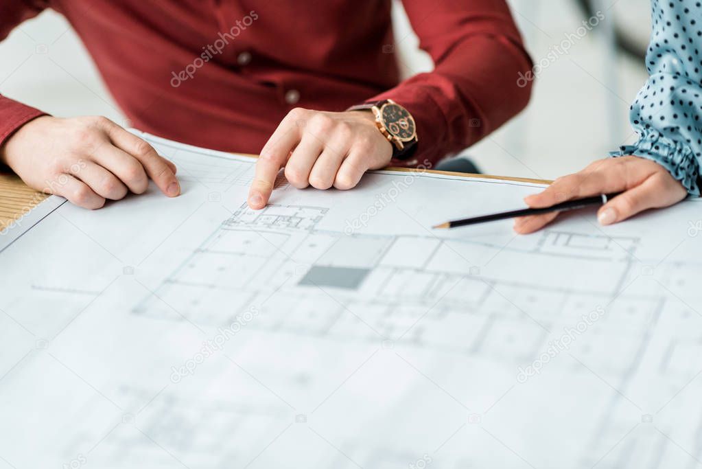 partial view of couple of architects working on blueprints in office