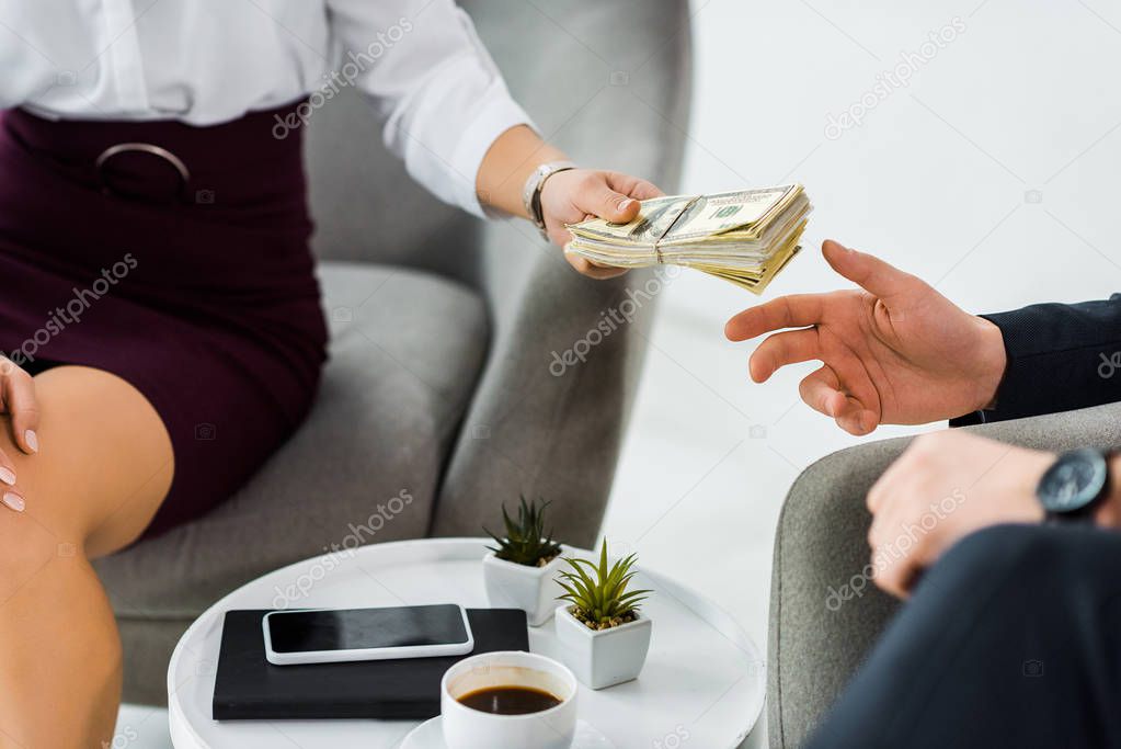 cropped view of businesswoman giving money to businessman in office 
