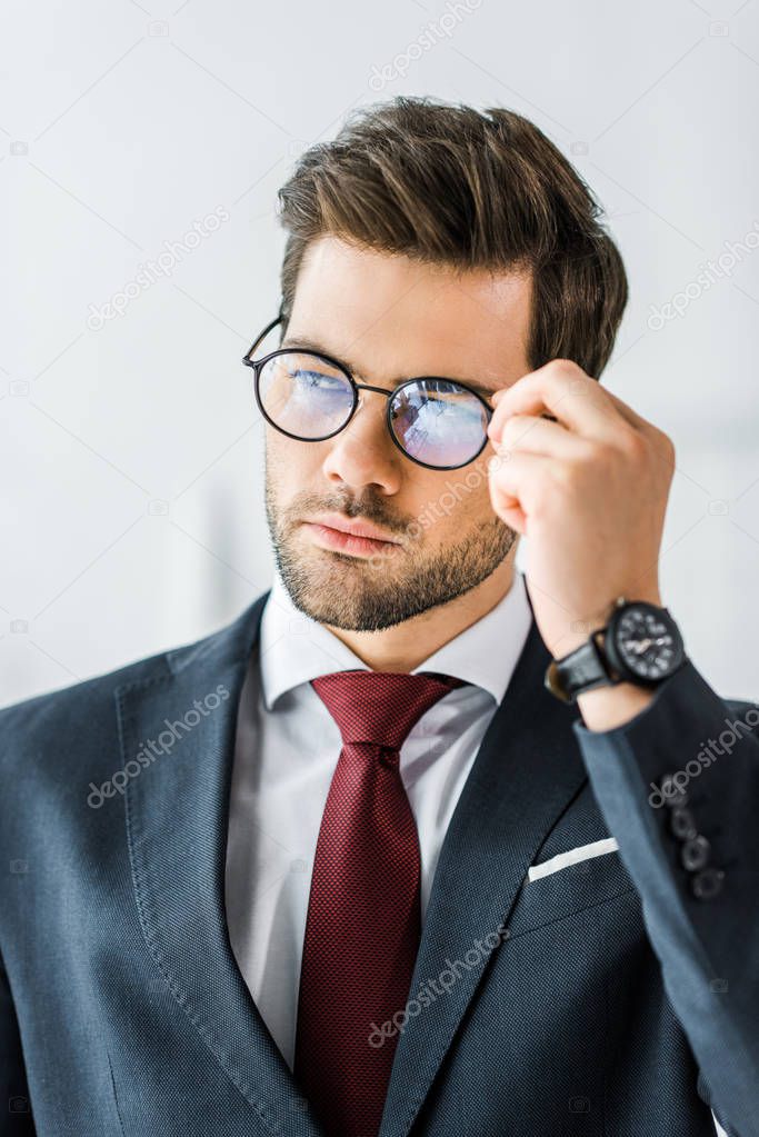 handsome businessman in formal wear adjusting glasses in office