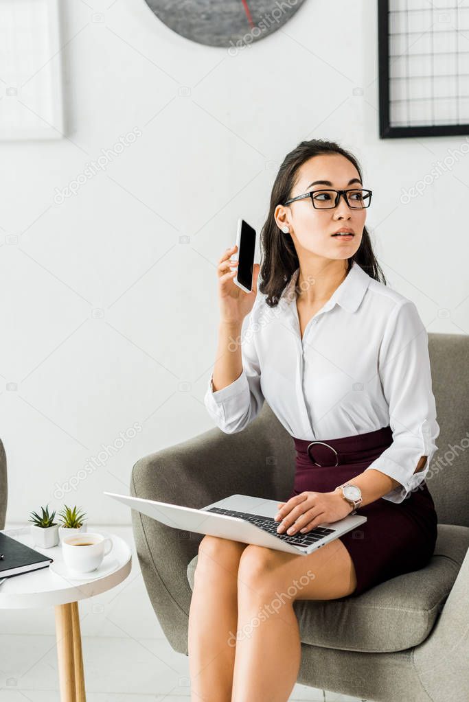 beautiful asian businesswoman sitting with laptop and using smartphone in office