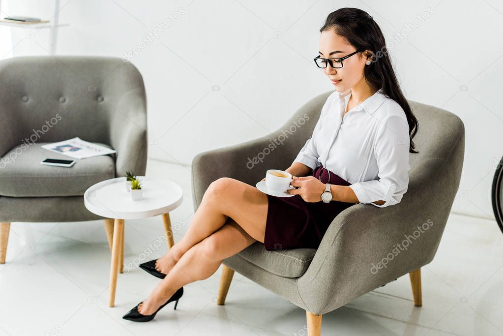 beautiful asian businesswoman sitting on armchair with coffee cup in office 