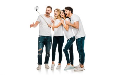 birlikte duran ve üzerinde beyaz izole smartphone ve selfie sopayla selfie alarak mutlu genç erkek ve kadın arkadaş