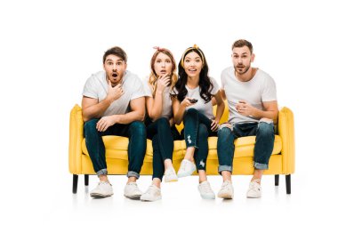 shocked young friends sitting on sofa with remote controller and looking at camera isolated on white clipart