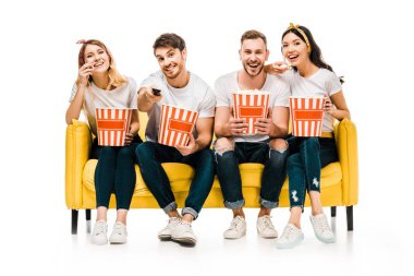 patlamış mısır kutuları tutarak ve üzerinde beyaz izole sarı kanepede otururken tv izlerken mutlu genç arkadaşlar  