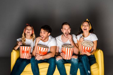 sarı kanepede oturan, film izlerken ve Grey kutularından patlamış mısır yemek neşeli genç arkadaşlar 