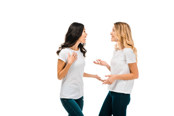 happy young women in white t-shirts talking and looking at each other isolated on white